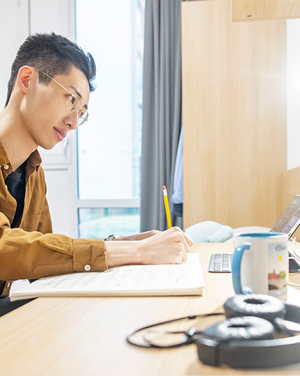 A student studying on a desk, in a clean, furnished bedroom.